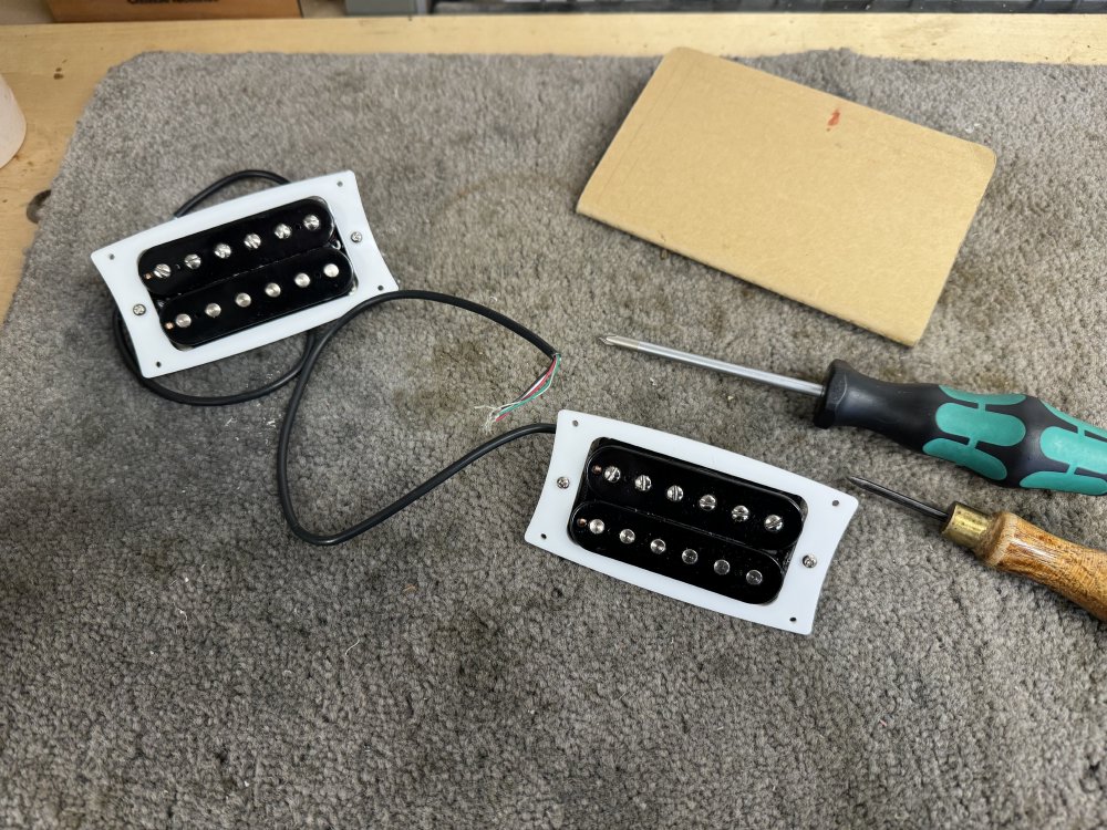 A photo of a pair of uncovered humbucker pickups with black plastic bobbins, mounted into white laser-cut acrylic mounting rings.