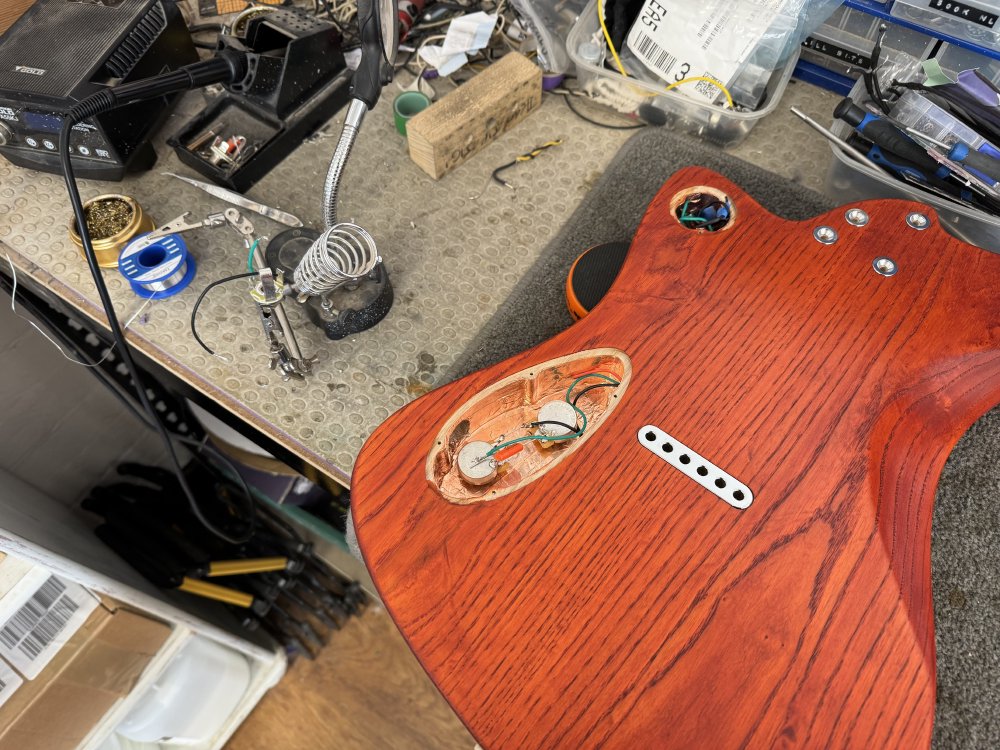 A photo of the back of the guitar focussing on the lower electronics cavity, in which you can see the two potentiometers in place, along with the capacitor for the tone control and some wires.