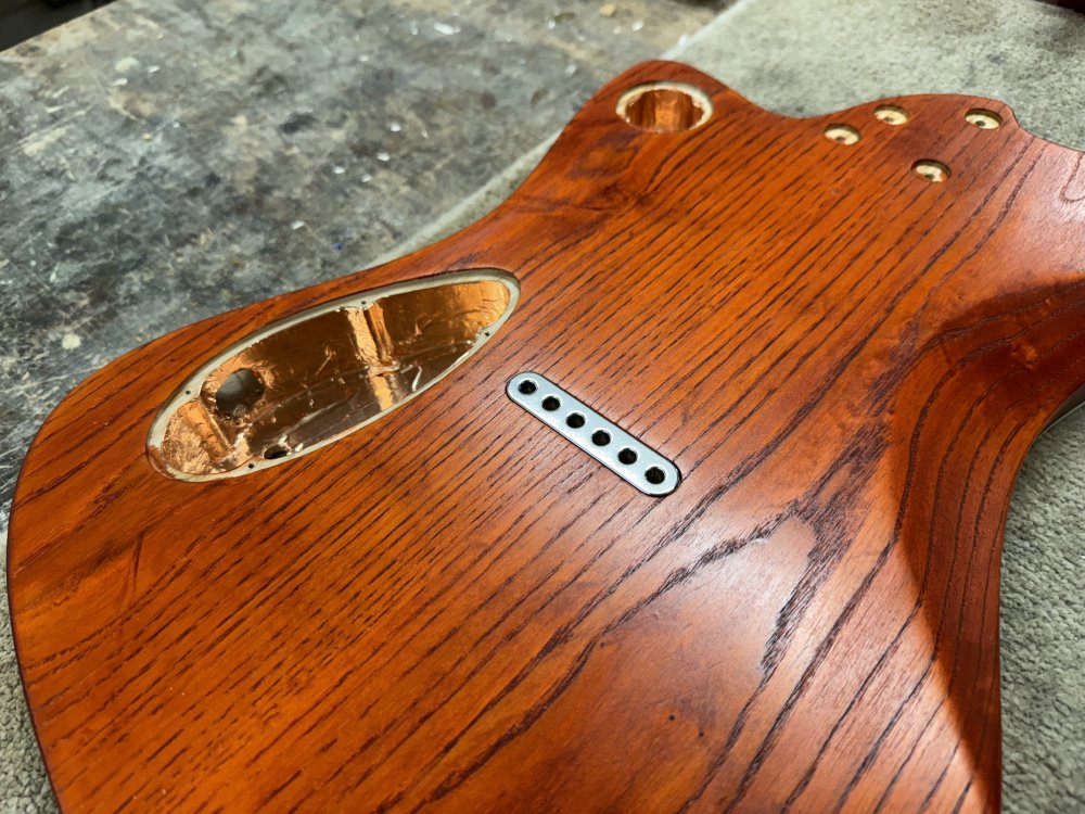 A photo of a guitar body again from the back, showing where the six individual thimbles where in the last picture, in this guitar there is a single piece of metal with six pockets in it.
