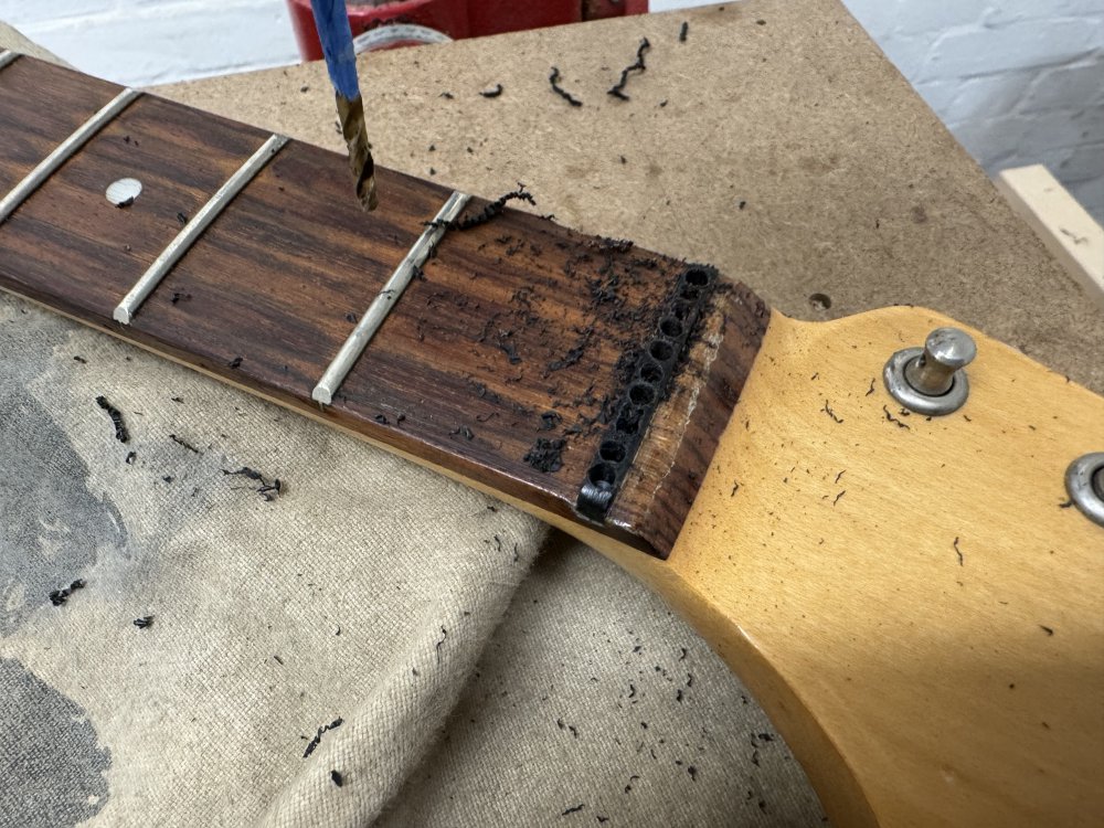 A photo of the plastic nut in the guitar neck, now with a lot of holes drilled in it perpendicular to the plane of the fretboard.