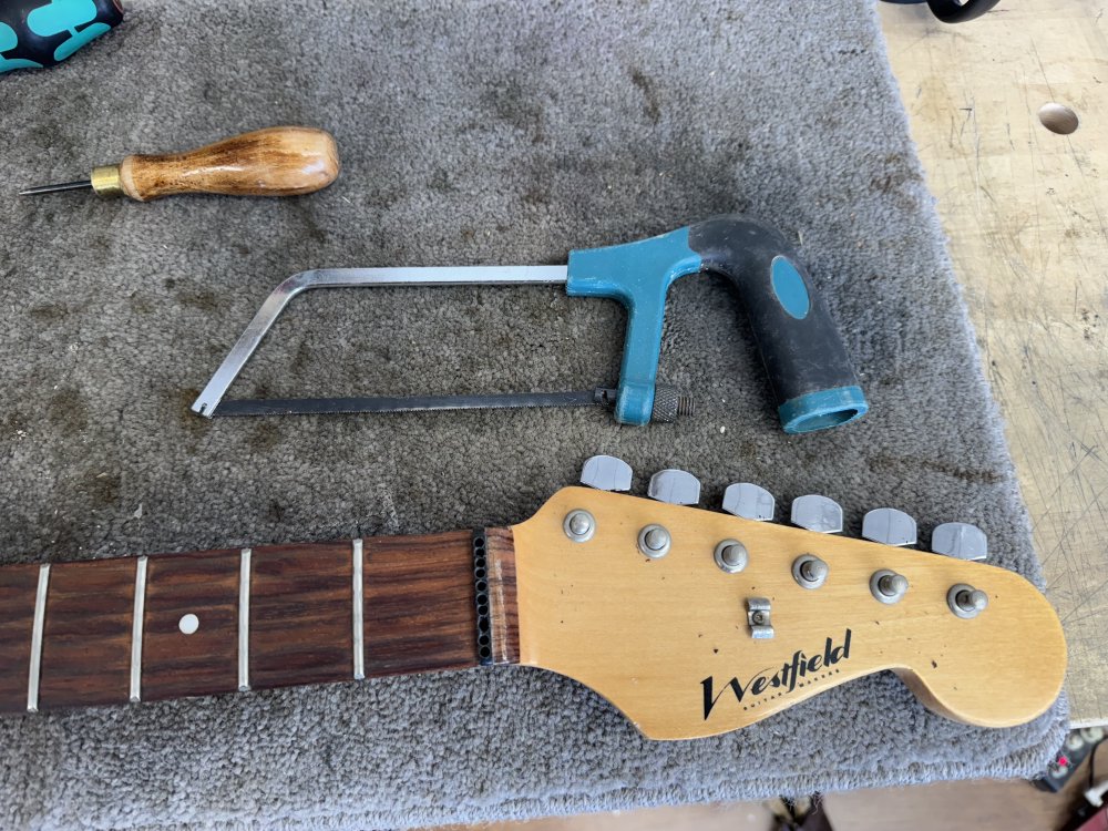 A photo of the drilled-nut in neck with a hacksaw next to the fretboard.