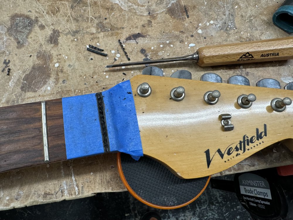 The neck again, and now there is some masking tape on the fretboard, and a small chisel next to it.