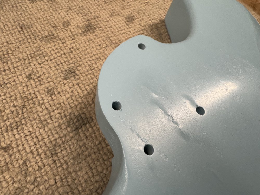 A photo of the back of the blue painted guitar from earlier, which shows that the paint has bulged up in a patch behind the neck pocket.