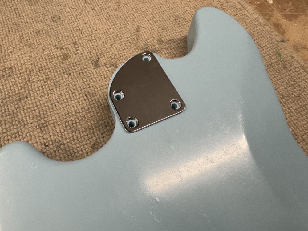 A photo of the blue guitar again, but showing the neck plate is covering the area where the paint has bulged.