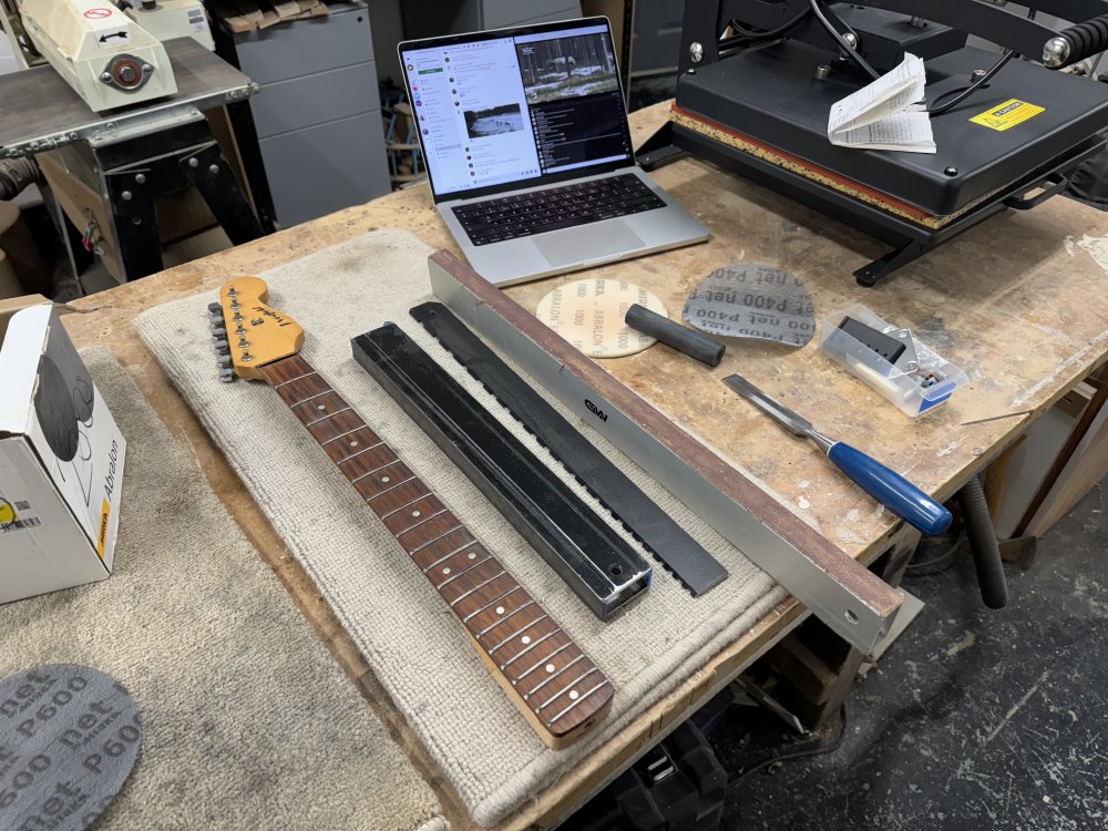 A photo of the strat-clone's neck on a workbench, next to which is a series of sanding bars and a notched ruler for checking the fretboard straightness.