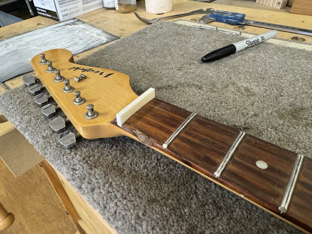 A view of a maple neck with rosewood fretboard with a block of bone in the nut slot.