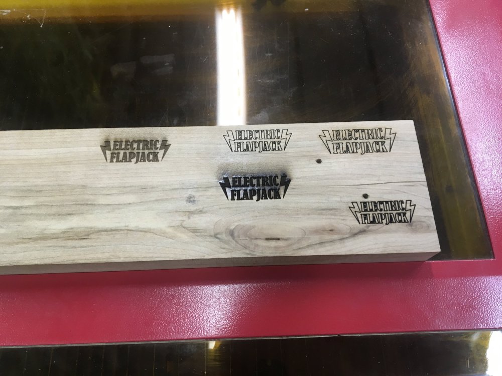 A plank of maple sits on the lid of the laser-cutter and you can see the Electric Flapjack logo has been etched into it at different power settings, creating lighter or darker burn marks as a result.