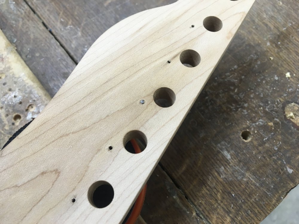 A close up of the back of a headstock, showing the holes where the tuners go, and the pilot holes for the screws that will secure the tuners. In one of those pilot holes is metal, the body of a screw who's head sheered off.