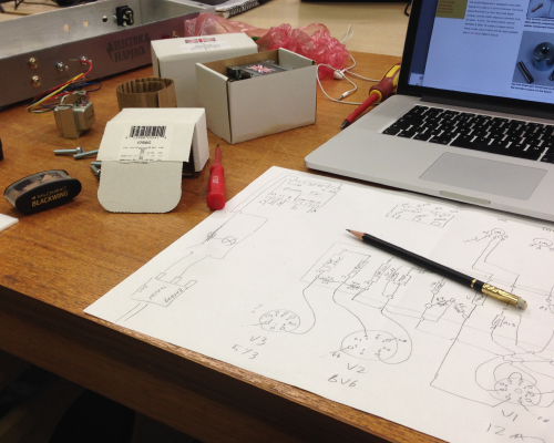 An A3 sheet of paper on a workbench next to a Mac laptop. On the paper is a crude circuit diagram of the amp circuit.