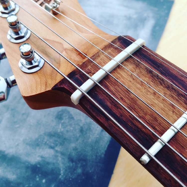 A close up of a guitar nut installed on the neck of a guitar. It isn't quite finished yet, as it hangs over the sides of the neck.