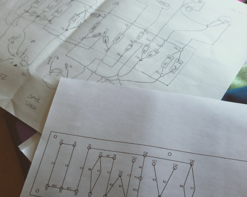 Bits of paper on a workbench, one of which is a hand drawn schematic for an amplifier, and the second is a printed schematic for the amp's turret board.