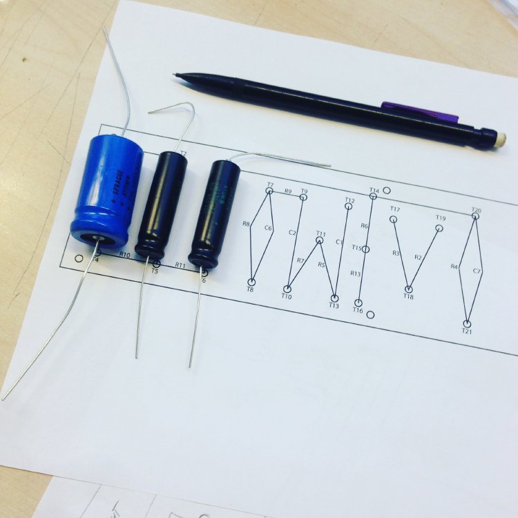 A photo of the printed turret-board schematic on a desk, with the capacitors and other components laid over it.