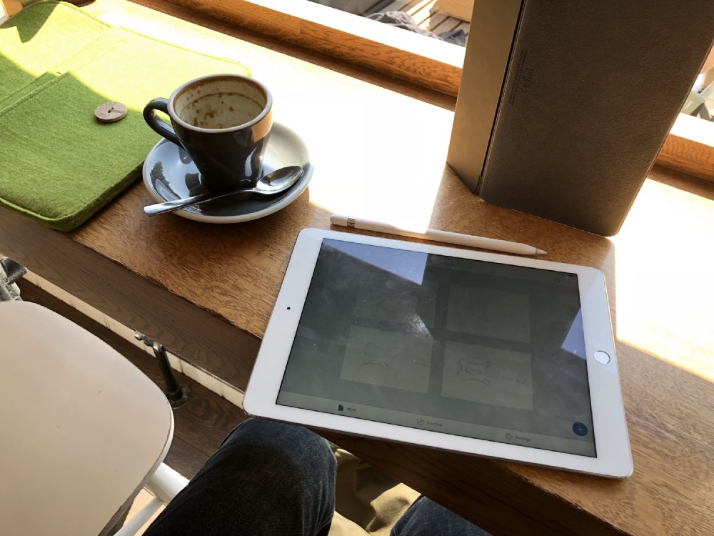 A photo of an iPad and a cup of coffee on a bench in a cafe.