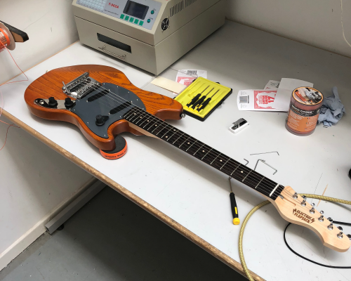 An orange guitar sites on the workbench looking close to complete.