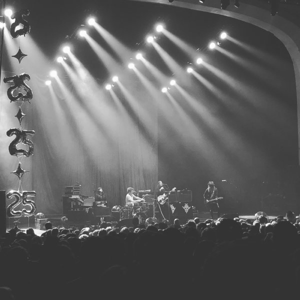 A photo of The Dandy Warhols on stage, with balloons that say '25' to the left of the stage.