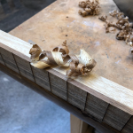 The side profile of a guitar neck being built, with some shavings on it from being planed. The shavings are two coloured, as both the dark wood of the fretboard and the light wood of the neck have been shaved.