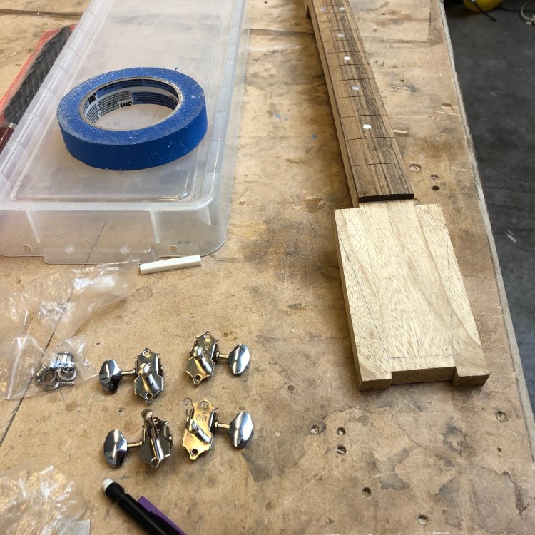 A close up of the squared shape of the headstock, with a pencil outline on it of where it's going to be cut into a more regular guitar headstock shape, tapering from the body end to the top. Beside it sit a set of open tuners.