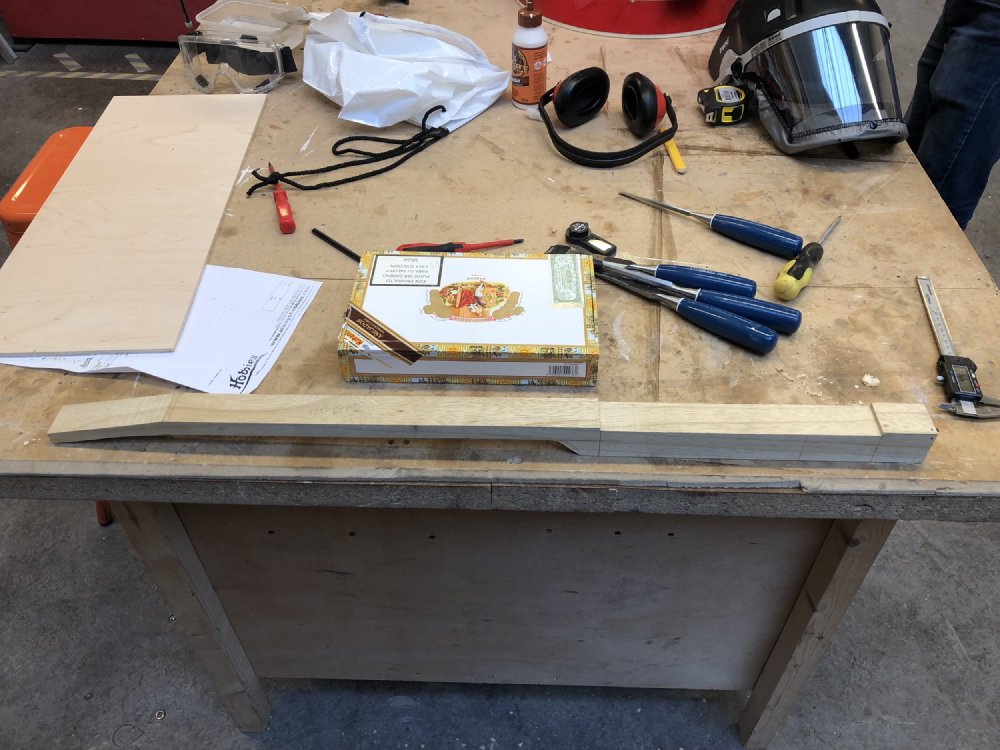 The core of a cigar-box guitar, the wood that makes the neck and runs through the box to the tail, sits on the workbench. You can see the various sections have been crudely cut into it.
