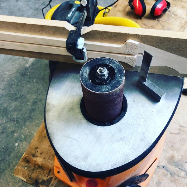 The neck in progress sits on the plate of a spindle-sander, waiting for the step left by  the bandsaw process to be rounded out.