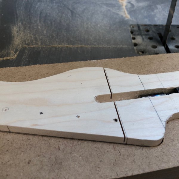 A close up of the headstock area of a blank of wood that has been profiled to be a guitar neck. There is a small cut, about 5mm deep across the face of it made with the bandsaw.