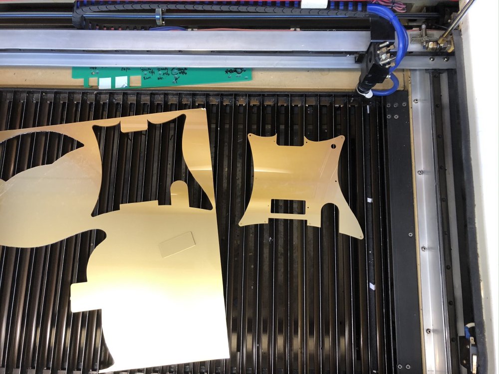 A photo of the bed of the laser-cutter, which shows some freshly cut gold-acrylic pick-guards.