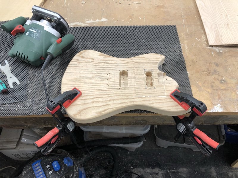 A photo of the halfway point: one pickup cavity is now neatly routed out, and the template is mounted over the second one ready to be cut.