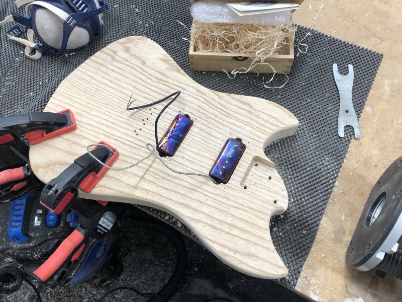 The guitar body sits on the workbench, router to one side, and in the pickup cavities sit a pair of min-humbucker sized pickups. The covers of the pickups are a mix of colours as the chrome cover has been heat treated to make it a mix of purple and yellows.