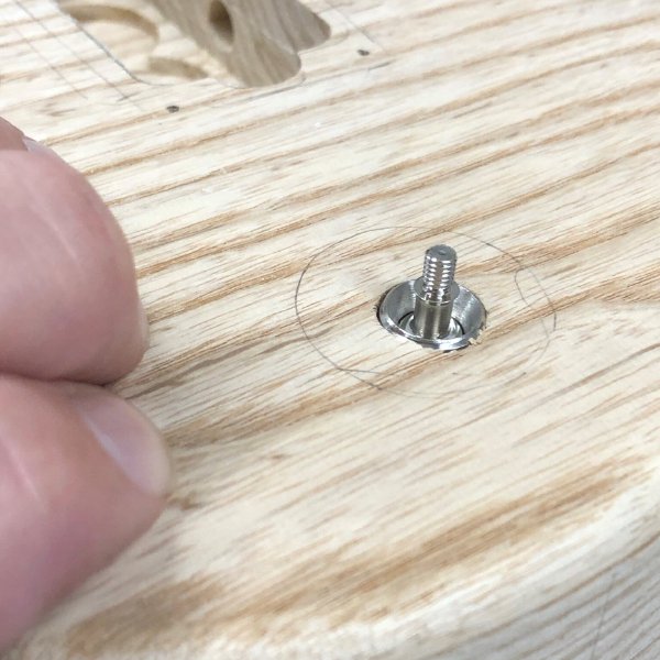 A close up of the top of the guitar body, where there is a small hole drilled for mounting the pickup selector switch. The switch is poking through, but not enough that the thread on the switch needed to mount it properly is visible.