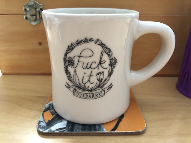 A coffee mug that has a nice floral design on it in which are written, in a script like font, 'Fuck It'