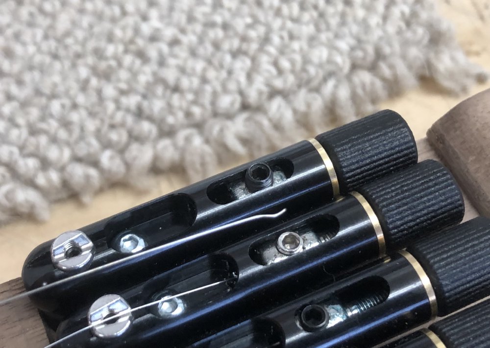 A close up on the bridge mounted 'submarine' tuners, and you can see one of the strings taken out of the tuner, which has a V shaped kink in it where the grub screw clamps it.