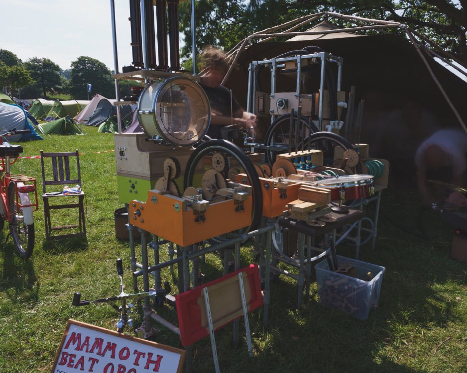 A weird looking contraption in the middle of a campsite: it seems to be made out of wood, a drum, bits of a bike, and many cogs.