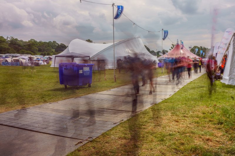 A long exposure shot of the main walkway through the EMFCamp festival site, showing the ghosts of people walking.