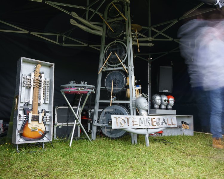 A somewhat steam-punk looking stand, with many maniquin heads, and a guitar trapped in a case and covered with solenoids.