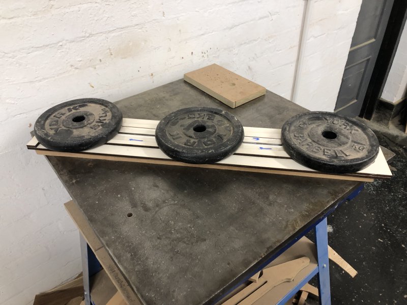 Three weight lifting disks sit upon the bits of wood I cut as the glue dries.