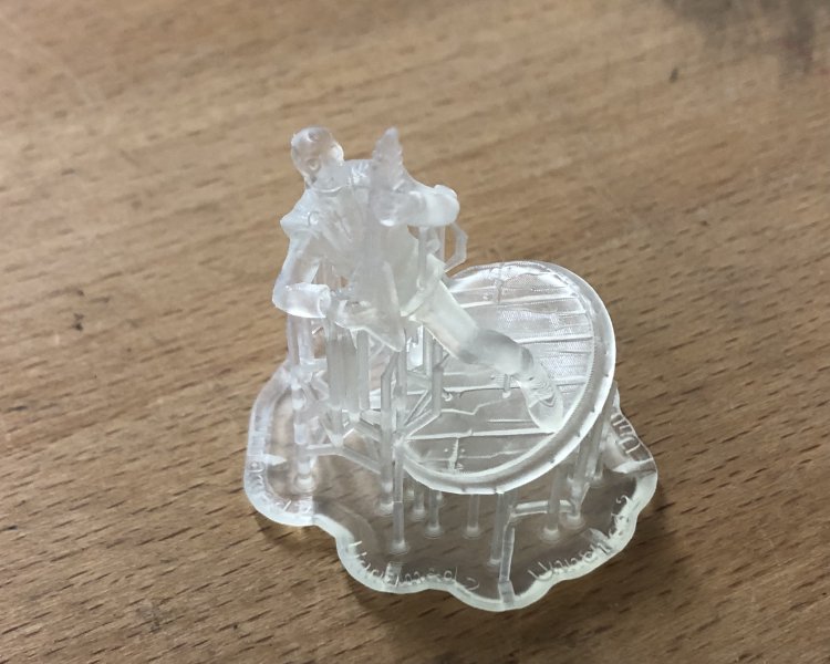 A photo of the same robot from the screenshot, but made from what looks like clear plastic, only with a lot of support structs around it left over from the 3D printing process. The detail is quite good, but not perfect given the small size of the print.