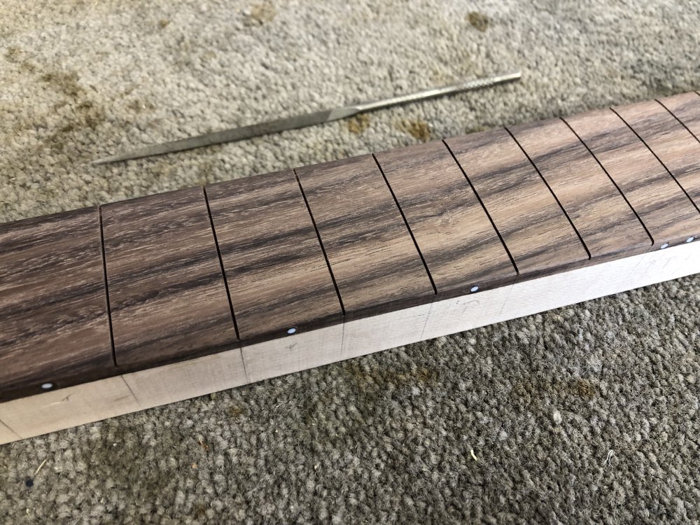 A close up of the fretboard showing the fret-slots, and the small long triangular file I used to widen the top of the slots next to the fretboad. You can't see the chamfer I've added, as slot is quite dark, I just hope people believe that I did this.