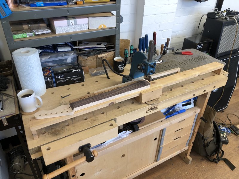 My workbench set up for the fretting process: in the middle is the arbor press, over which has been placed a wooden jig that holds the neck level, letting you slide the frets under the press whilst keeping things level.
