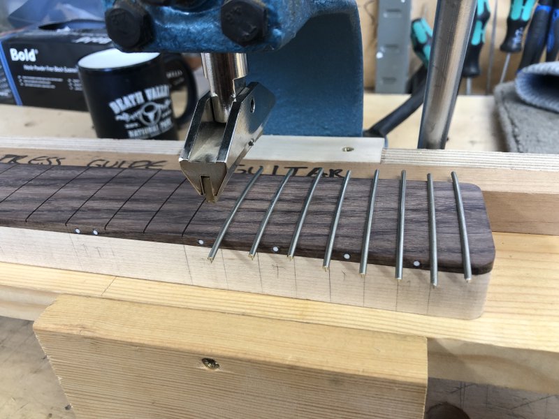 A close up of the neck under the press, with eight frets already pressed in to their slots.