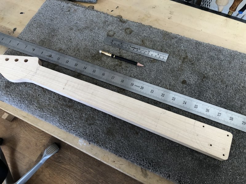 The neck is sat fretboard side down on my workbench, revealing the unfinished rear, still square edged from being cut from the original wood. On the back is a bunch of pencil marked lines to guide me when I carve the back of the neck, and you can see the ruler and pencil beside it.