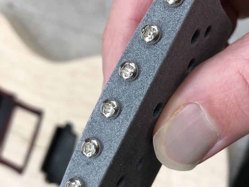 A close up of my 3D-printed bridge showing the heads of the screws that connect to each string sandle. Each screw has the familiar cross of a philips screw head, but an extra dimple on the face positioned between two of the cross blades.
