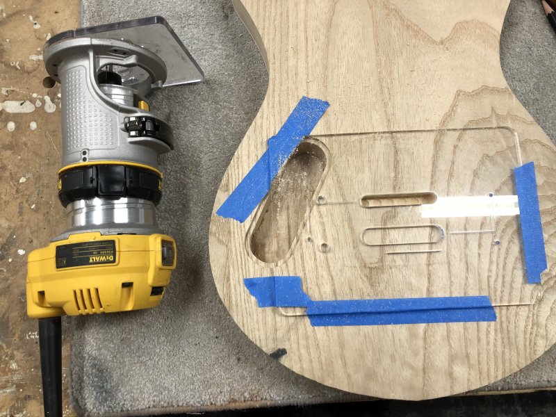 The guitar body on the workbench with a plam-router next to it. The area where the string-holes were is now a single lozenge shaped cavity.