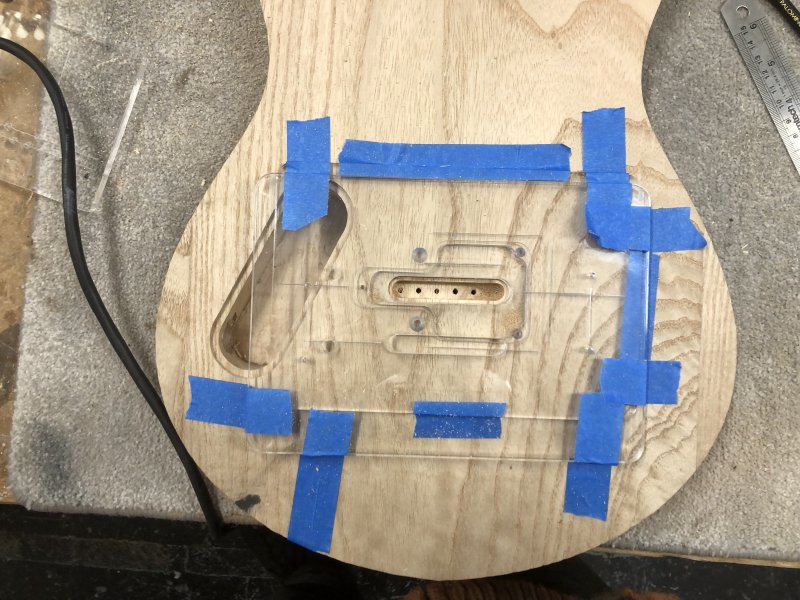 A slightly hard to disambiguate picture of two templates both cut in transparent acrylic stacked on atop the other and taped to the guitar body.