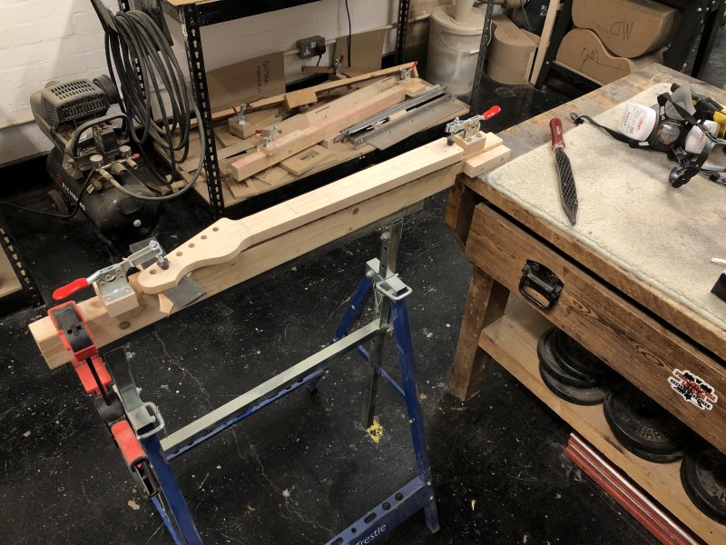 The neck is on a jig on a trestle stand, and beside it is a workbench with a saw-tooth rasp ready to be used.