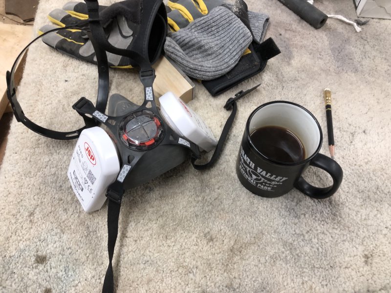 A respirator mask and a mug of black coffee sit on a workbench, each one competing for the lower half of my face.