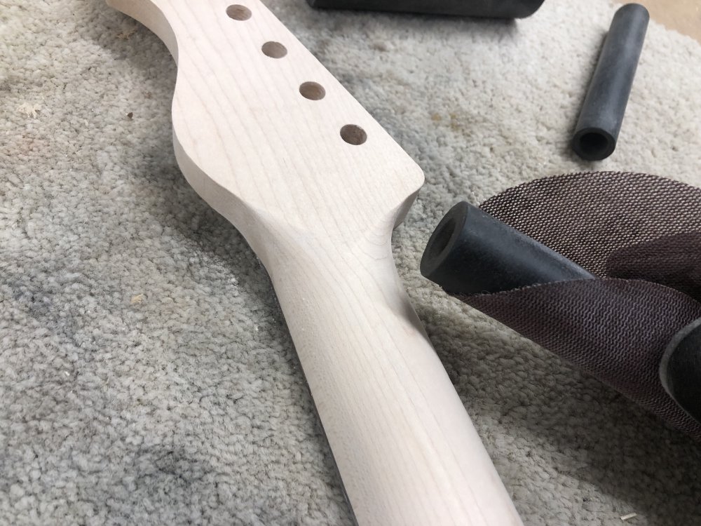 A close up of the transition between the main part of the back of the neck and the headstock, and you can see my hand holding a black rubber tube around which is wrapped a sanding disk.