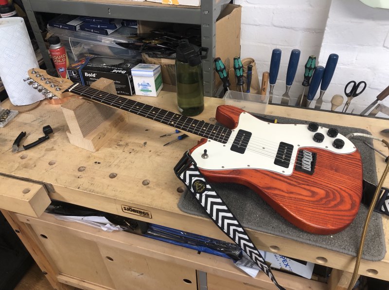 A bright orange guitar sits on a workbench surrounded by tools.