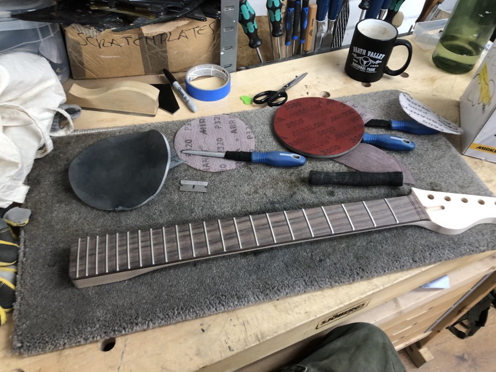 The neck is now on a messier workbench, surrounded by files as before, but also sanding disks, a razor blade, scissors, and a cup of tea.