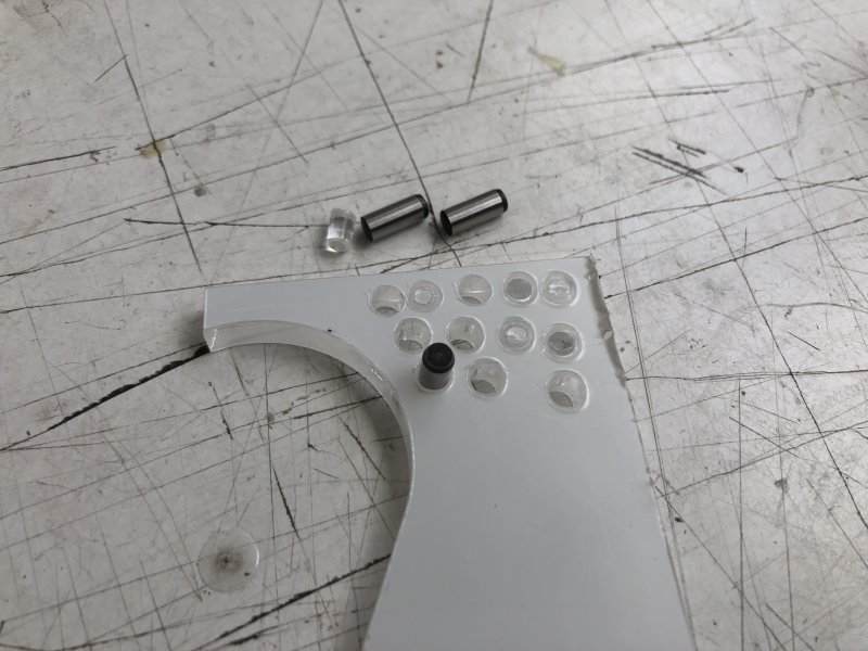 A piece of acrylic with many holes cut into it (some of which are just outlines as the cut didn't go all the way through). Some metal pins sit beside the acrylic and one is stuck into one of the holes.