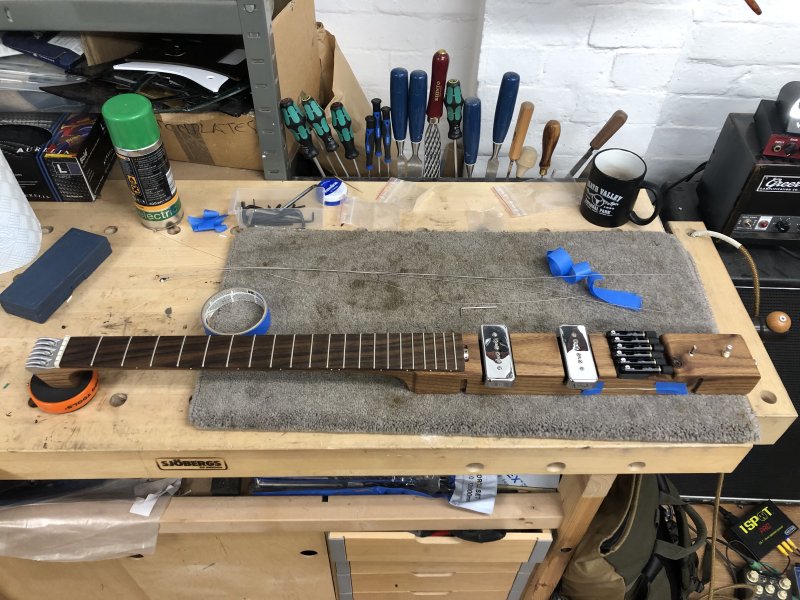 The core of the älgen guitar sits on the workbench, which is a single long piece of wood consisting the neck and the core of the body, just missing its 3D printed wings and strings.