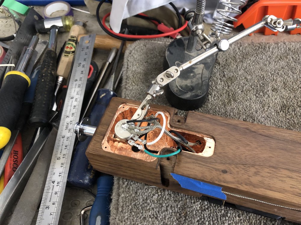 The guitar is on its front on the workbench, with the electronics all exposed as I try to unsolder the old volume control to install the working replacement.